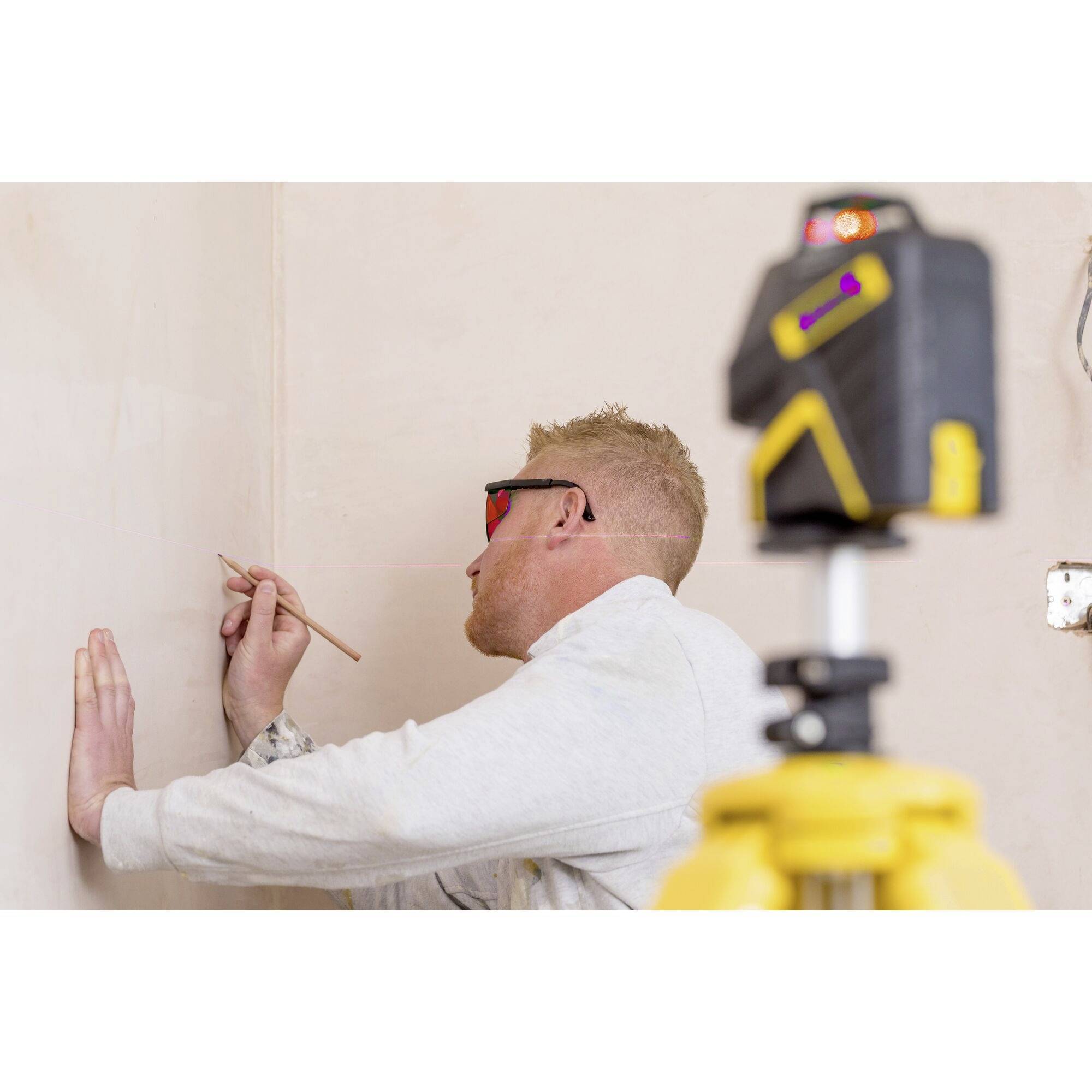 A man is wearing safety glasses and measuring the wall height in a room using a laser measuring tool, likely for construction or renovation work.