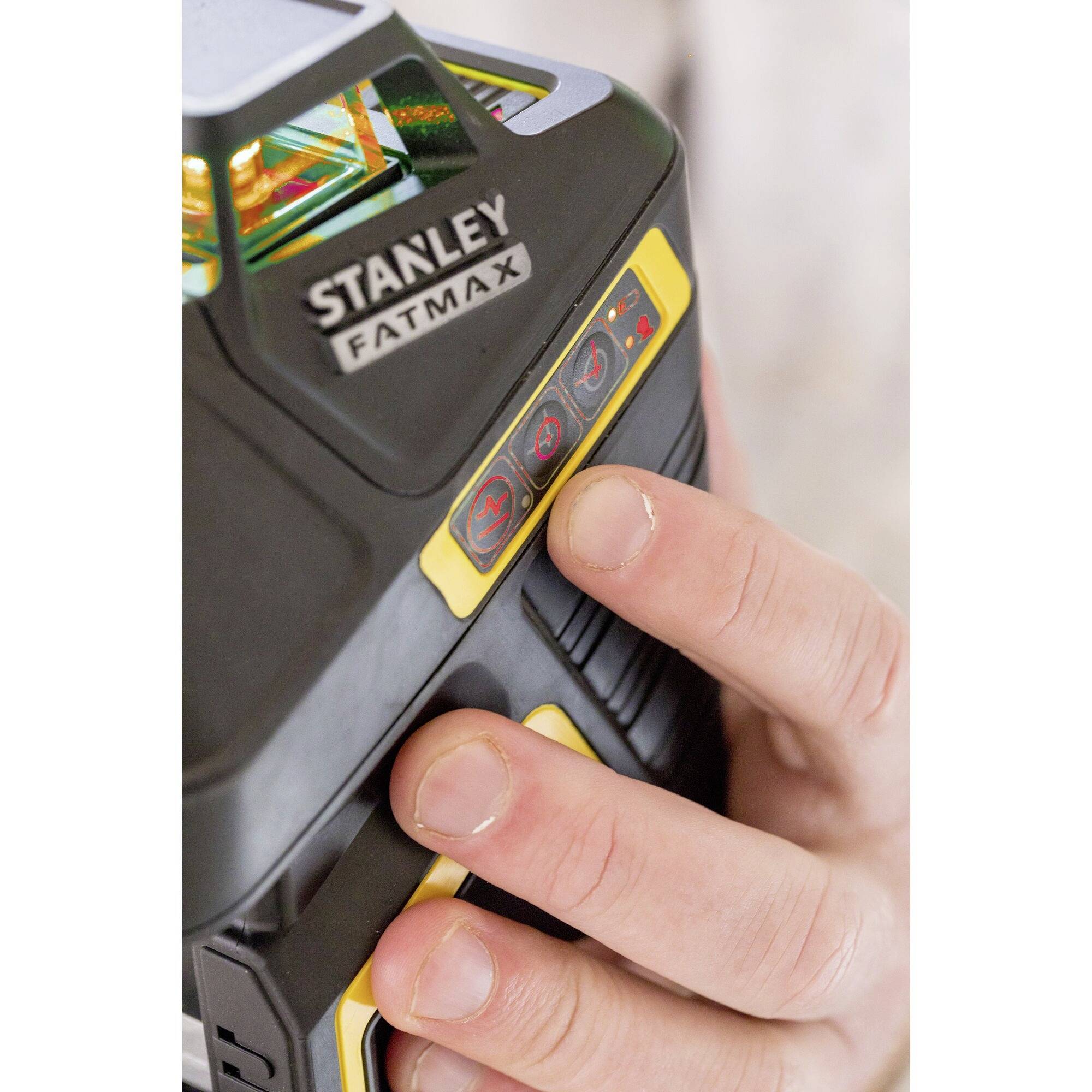 A hand is holding a Stanley Fatmax device. The hand is pressing yellow buttons on the side of the device, next to illuminated indicators.