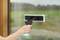 A hand is cleaning a window with a squeegee and spray cleaner. In the background, a blurry green garden can be seen.