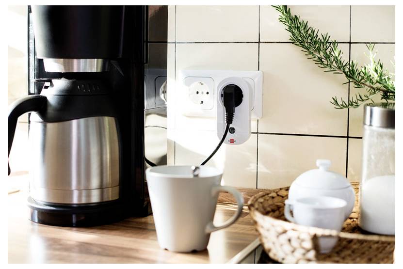 Coffee maker with plugged-in electric kettle, mug, and kitchen items on a countertop beside a wall outlet.