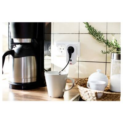 Coffee maker with plugged-in electric kettle, mug, and kitchen items on a countertop beside a wall outlet.