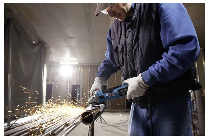 A person uses an angle grinder to cut metal pipes, creating sparks in a workshop setting.