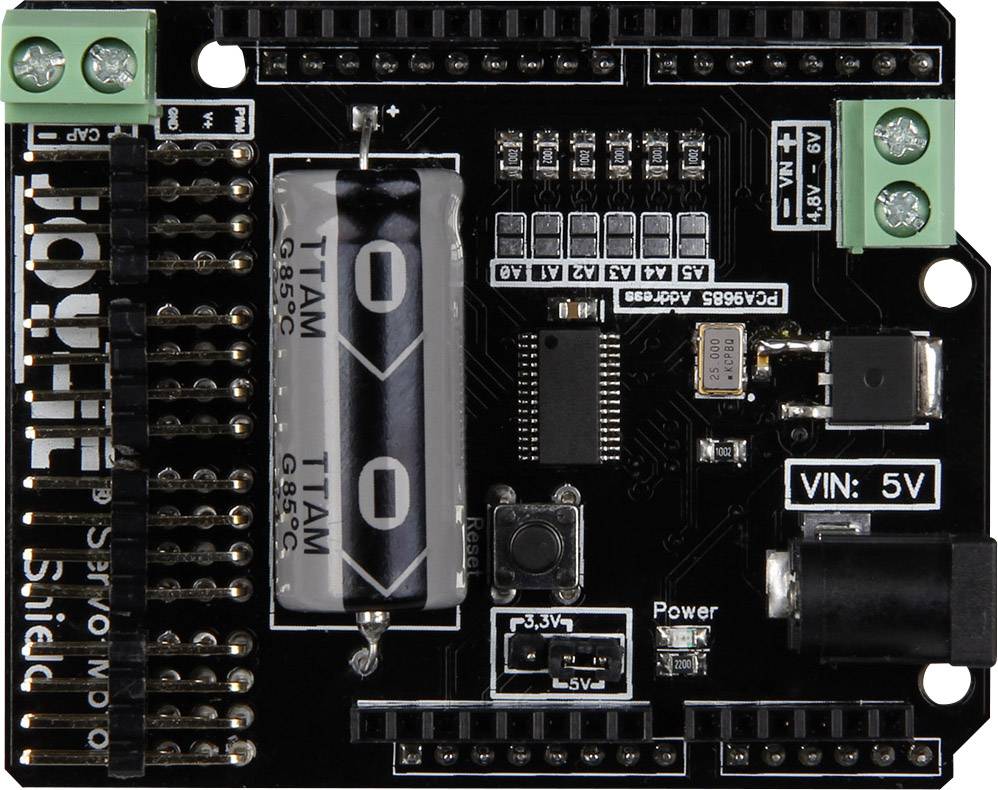 A black circuit board with electronic components, including a large capacitor, multiple slots and small chips.