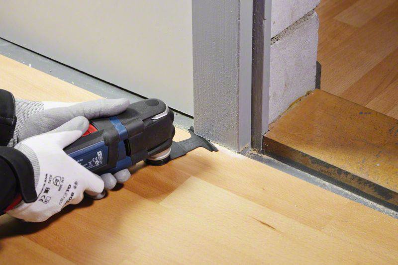 A person is cutting the bottom part of a door frame with an electric multi-purpose tool to adjust the flooring.