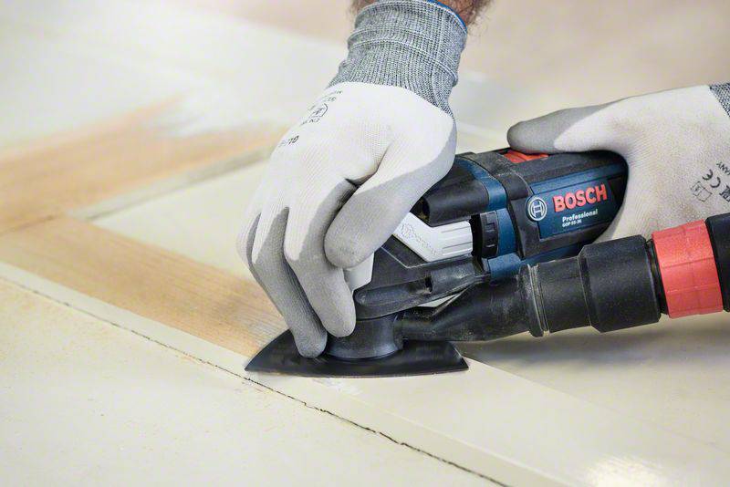 A person is sanding a wooden surface with a Bosch multi-tool. The person is wearing gloves for safety.