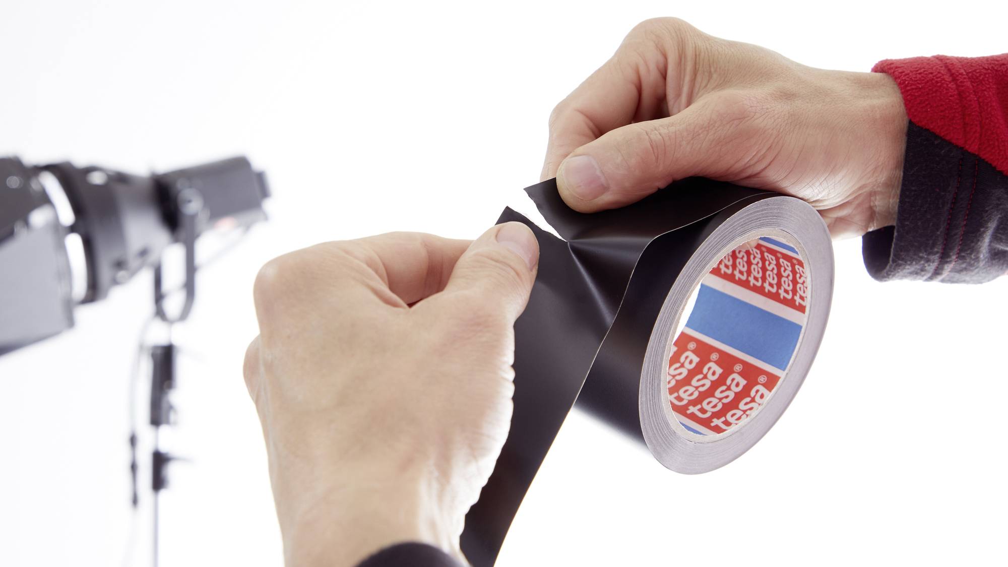 A person is holding a roll of black adhesive tape in front of a lighting device.