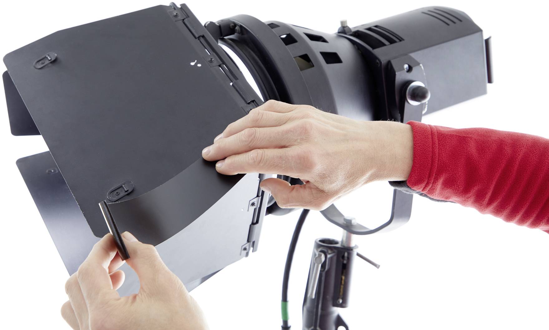 'Hands of a person adjusting the flaps of a studio light to shape the beam. Shot in a bright studio.'