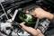 A person is holding a smartphone over an open bonnet and displaying an image of a part of the engine on the screen.