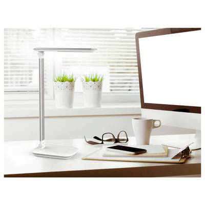 'A modern desk setup with a sleek lamp, a computer monitor, a white coffee cup, eyeglasses, and a notepad on a light-colored table.'