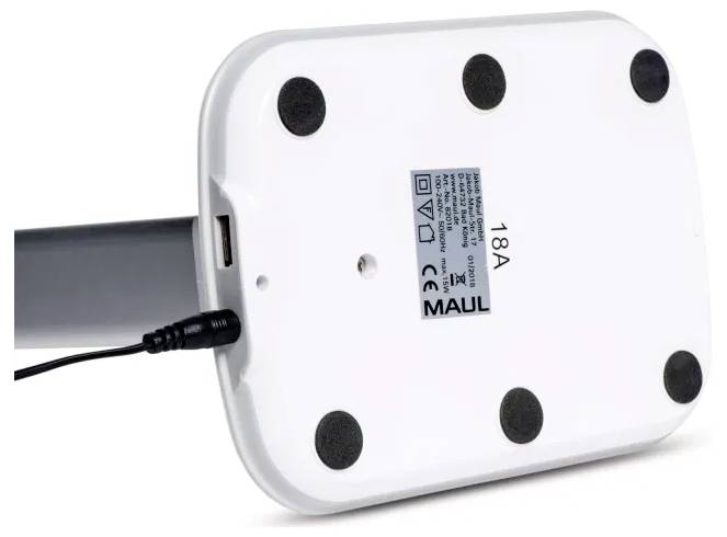 The image shows the underside of a white rectangular base of a desk lamp featuring a power cable, six black rubber feet, and a label with text.