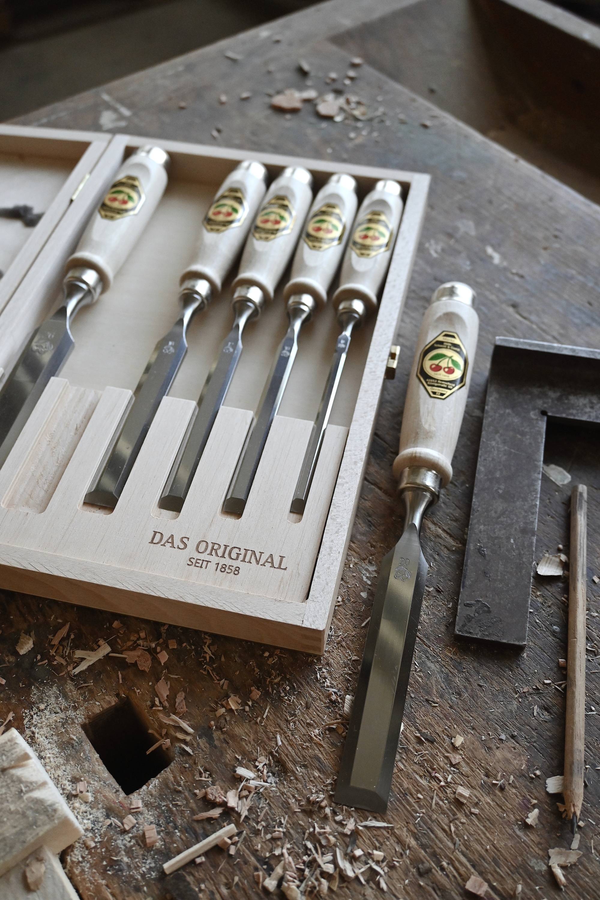 Toolbox with seven fine cutting chisels, neatly lined up. Inscription: 'THE ORIGINAL SINCE 1858'. Wood shavings in the background.