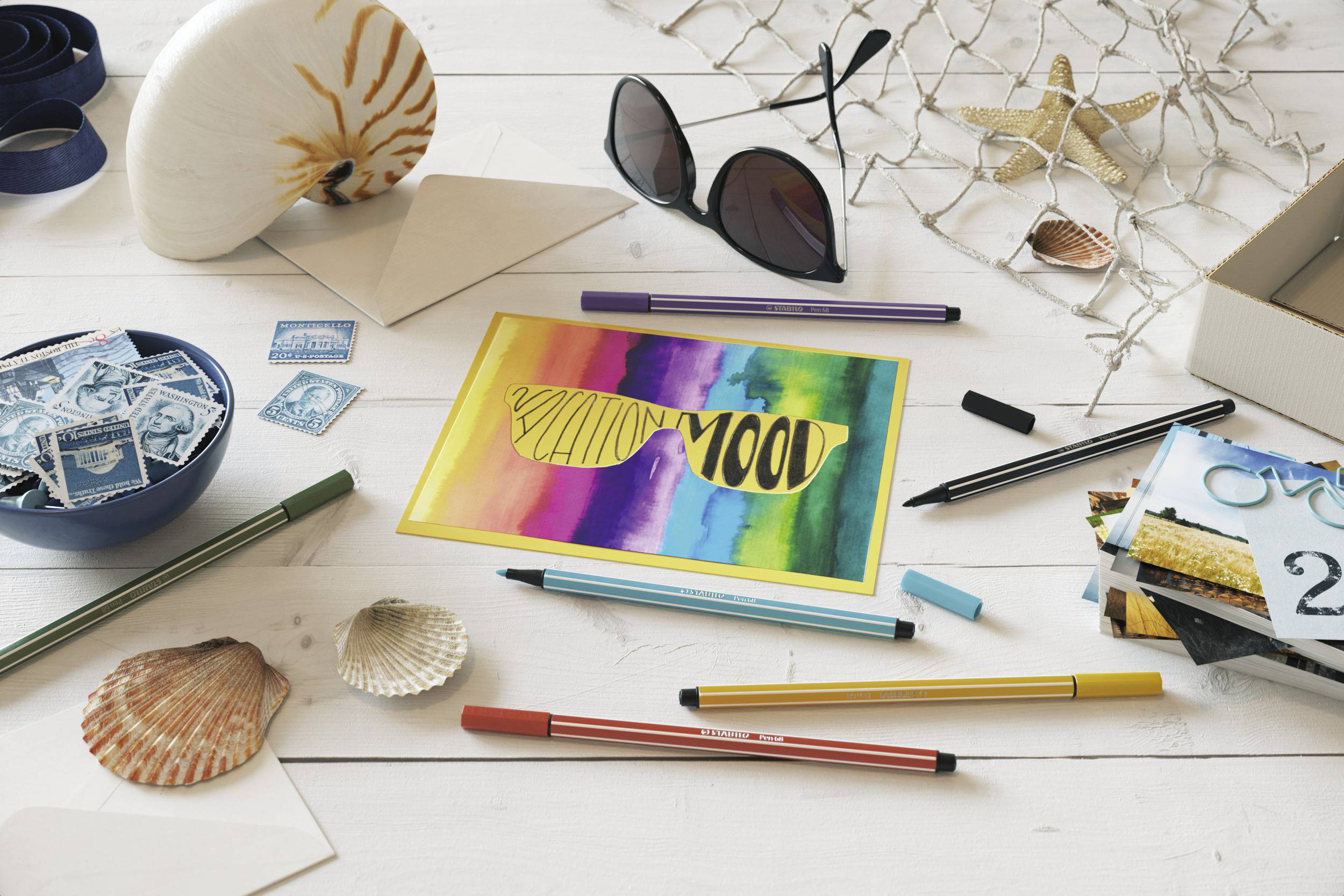 A white wooden board with sunglasses, seashells, stamps, pens and a postcard displaying 'Mood' in colourful letters.