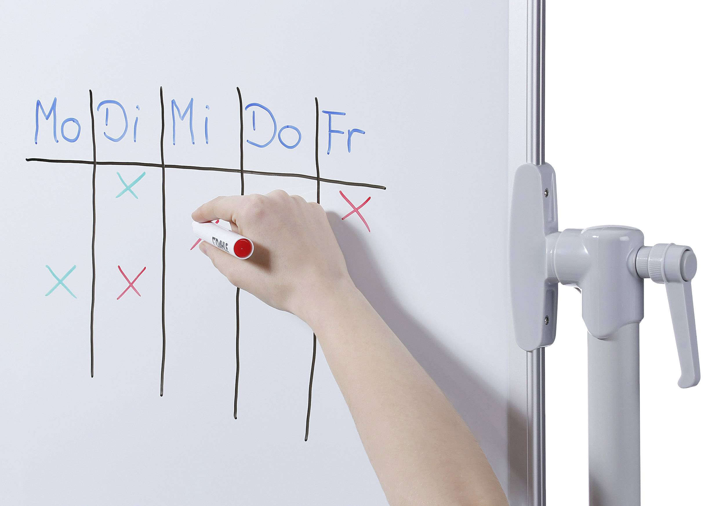 A hand writes an 'X' in red pen in a table on a whiteboard, with days of the week as column headings.