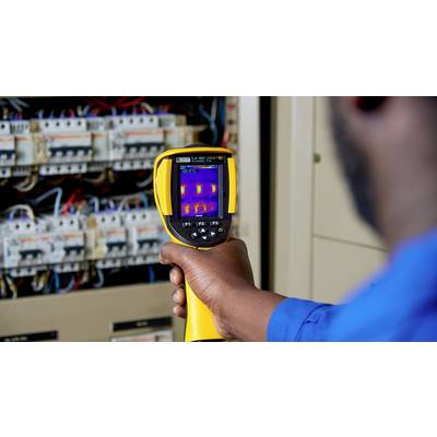 A person is using a thermal imaging camera to check electrical junction boxes for hot spots. The screen displays several coloured points.