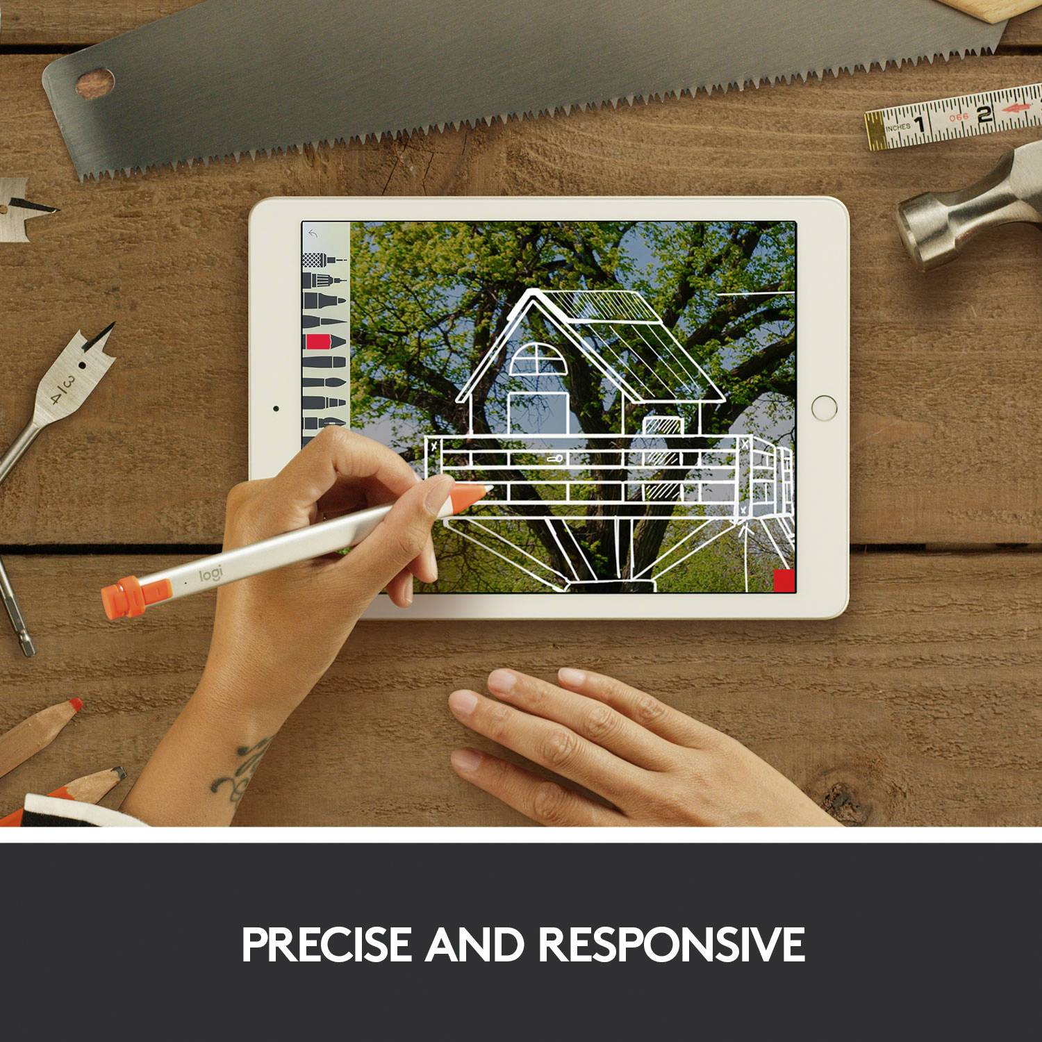 A person is drawing with a pen on a tablet, which displays a sketch of a house. Tools are lying on a wooden table in the background.