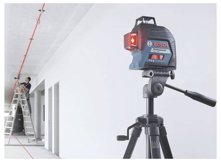 'A laser level on a tripod projects a straight line on the ceiling; a person stands on a ladder adjusting fixtures along the line.'