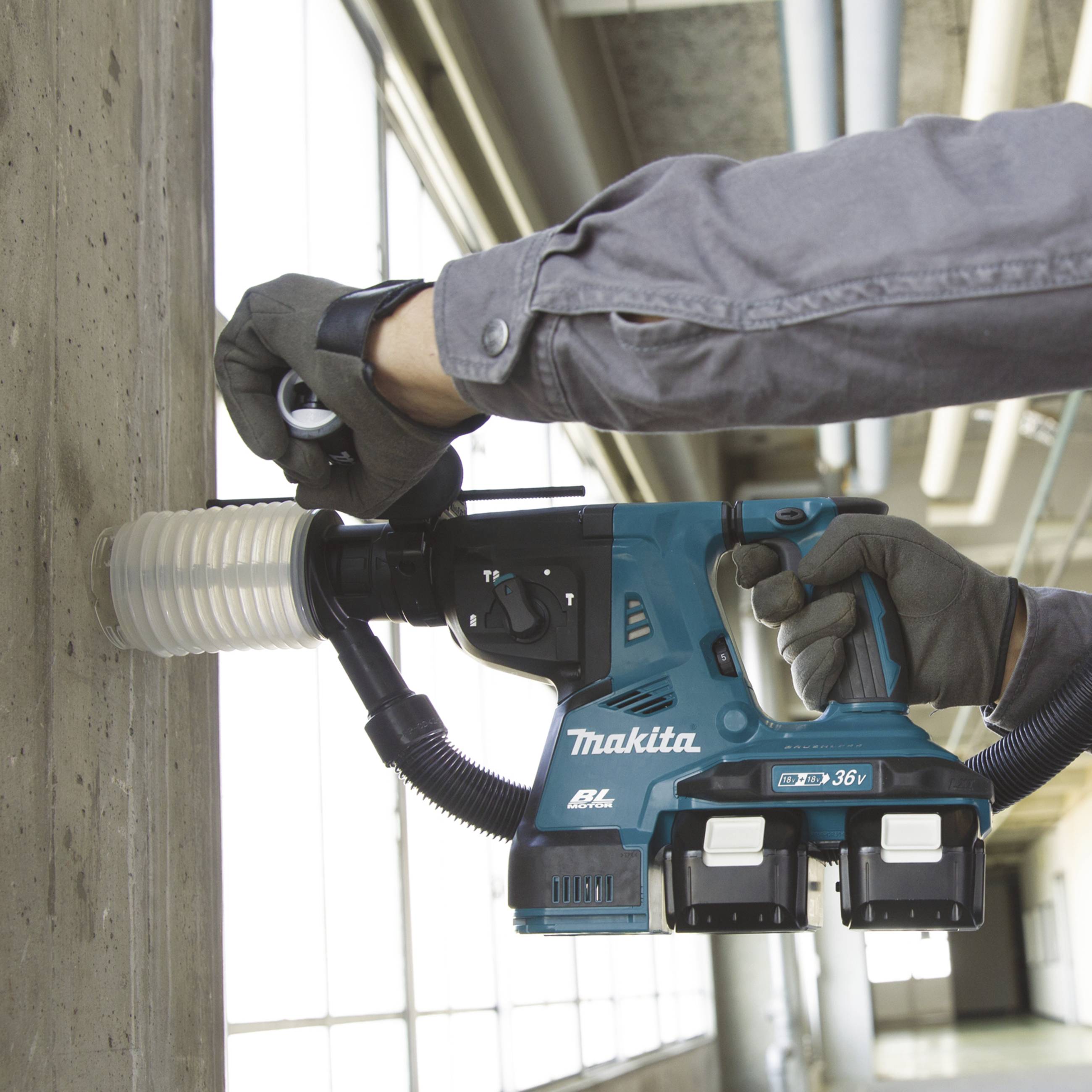 A person is working with a cordless drill hammer on a concrete wall. The device is a 36V model with two batteries.
