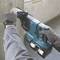 A worker is drilling into a concrete wall with a blue hammer drill. The hammer drill has two attached batteries and dust extraction.