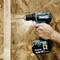 A blue cordless drill with a battery attached is drilling a hole into a wooden board. A hand is holding the drill steady during use.