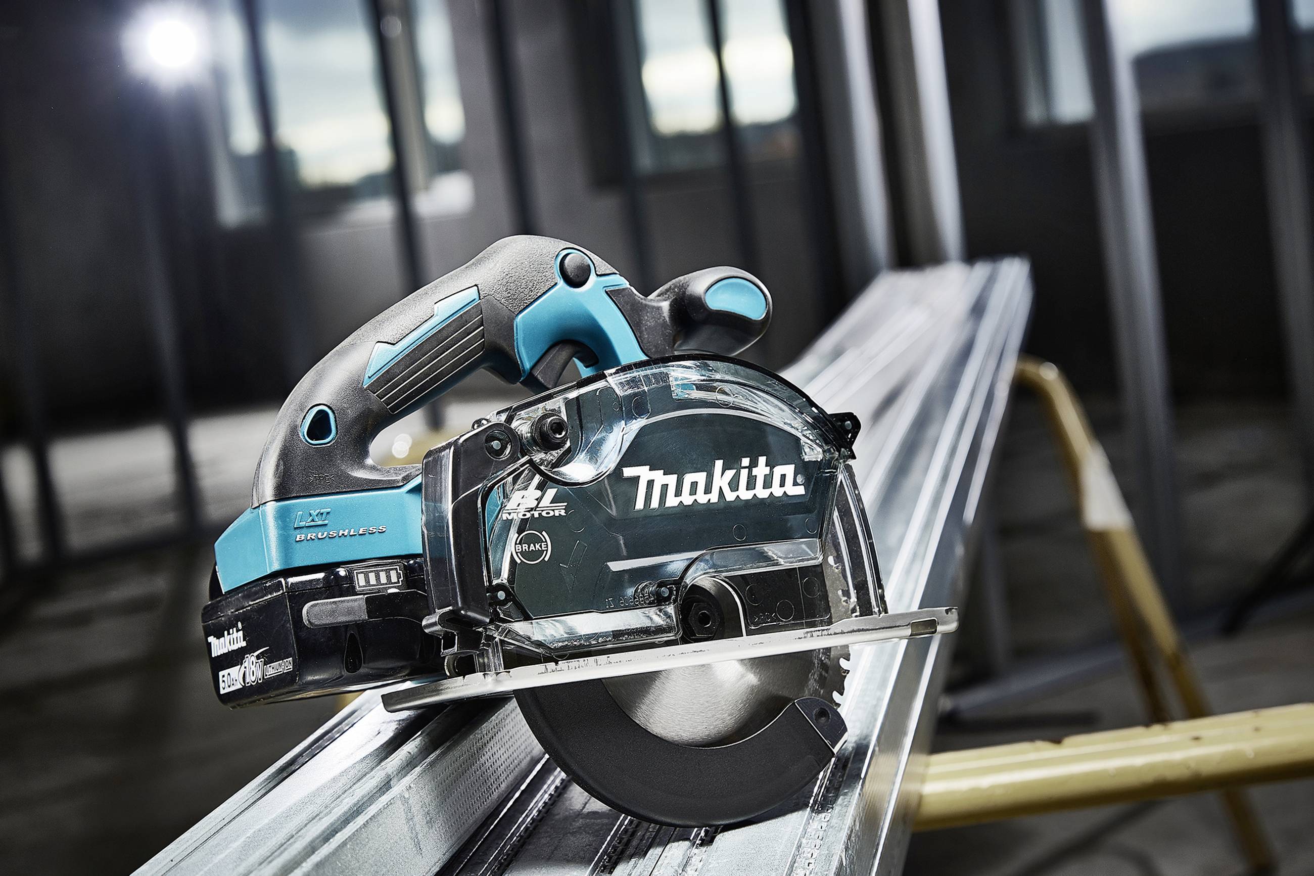 A Makita circular hand saw cutting through a metal piece, closely captured in a workshop environment with a blurred background.