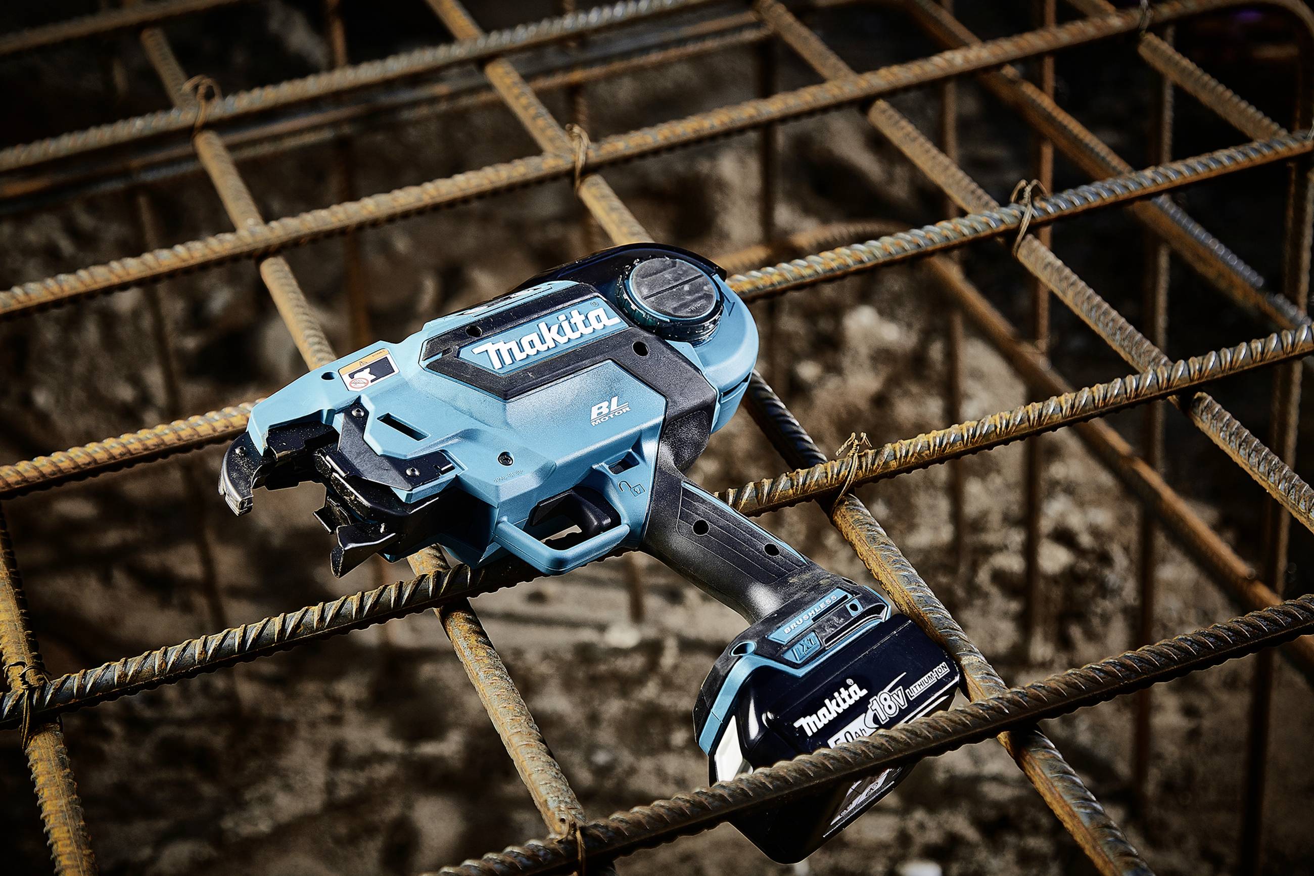 A blue wire binding machine by Makita is placed on a steel mesh grid, used for construction work.