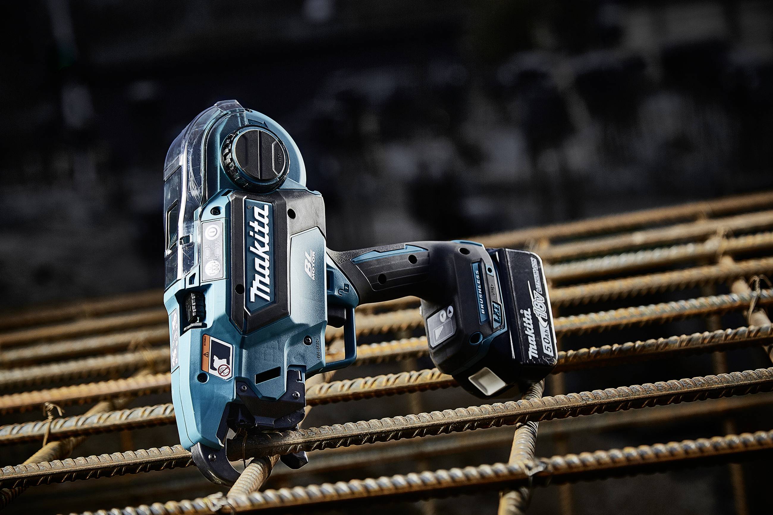 A battery-powered angle grinder in turquoise sits on reinforcing steel bars, suitable for construction work or metalworking.