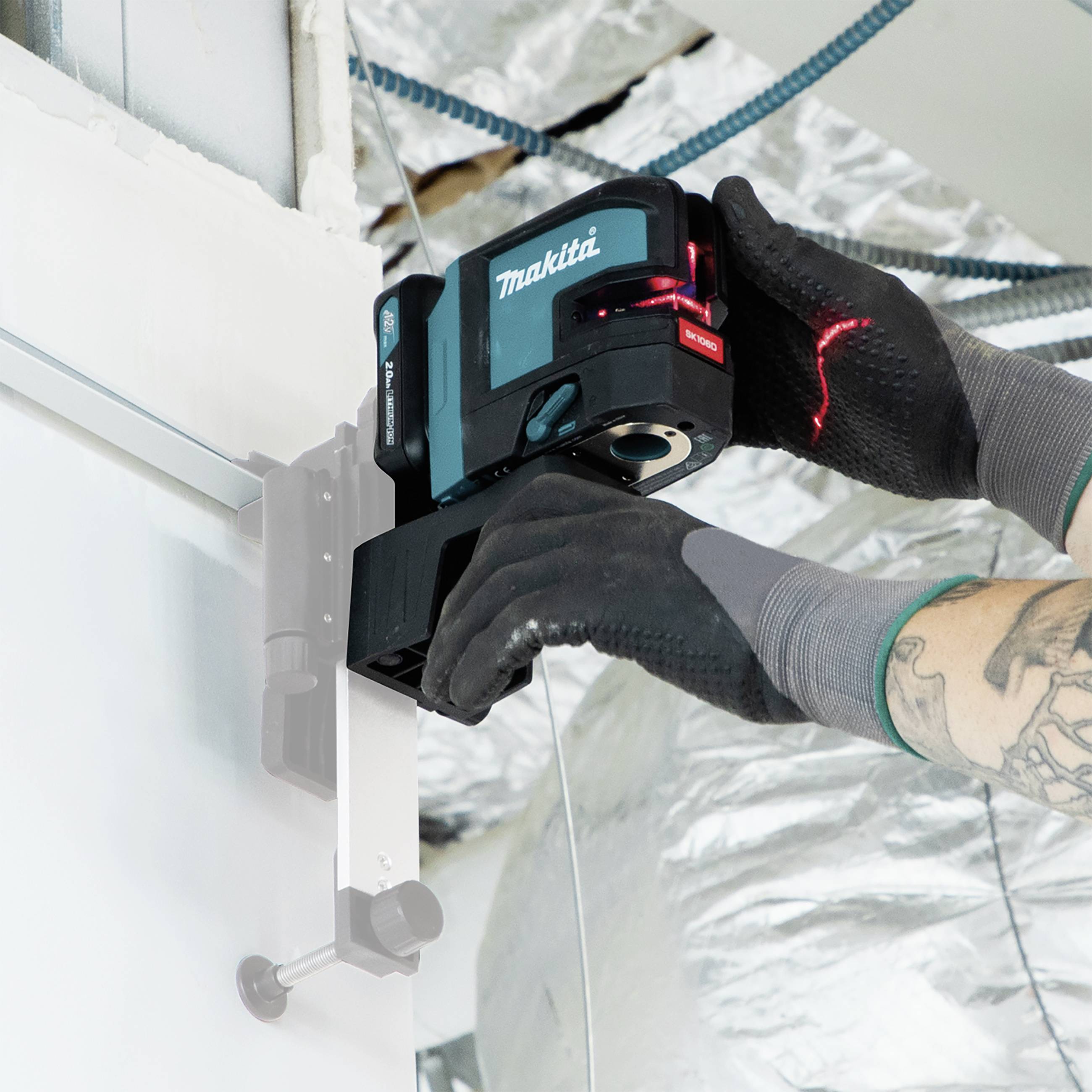 A person is using a laser device branded 'Makita' to carry out precise measurements on a wall.