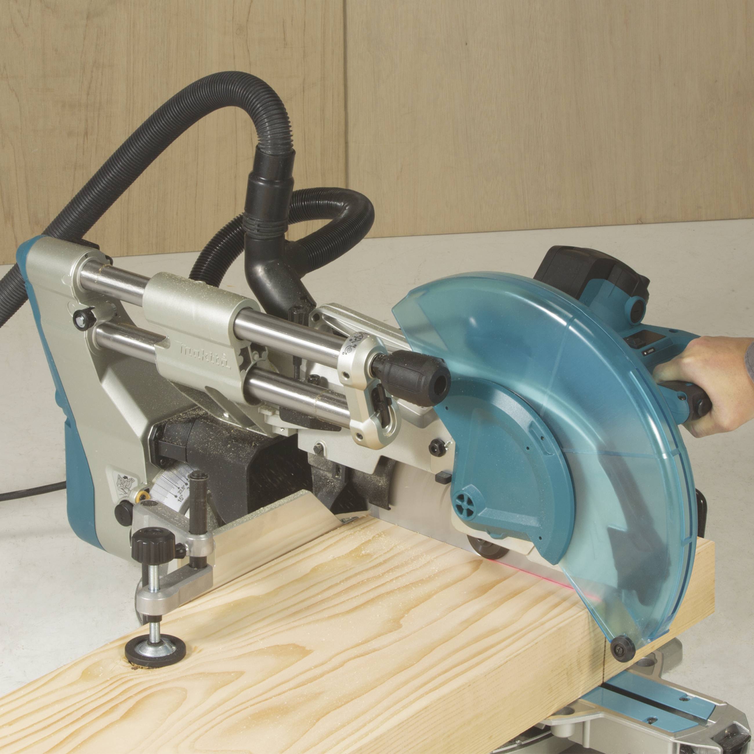 A blue electric chop saw is cutting a piece of wood. The saw has a guard, and the surroundings are a workshop.