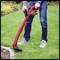 A person is cutting the lawn with a red, electrically powered lawn trimmer. The lawn is green and well-maintained.