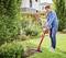 A man is mowing the lawn with a red lawn trimmer in a well-maintained garden next to a house.