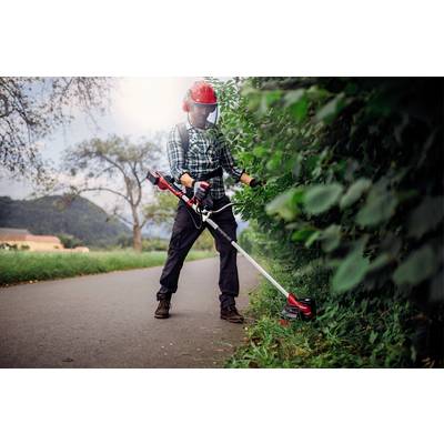 A man wearing a safety helmet and visor is trimming grass along the roadside with a strimmer in a rural setting.