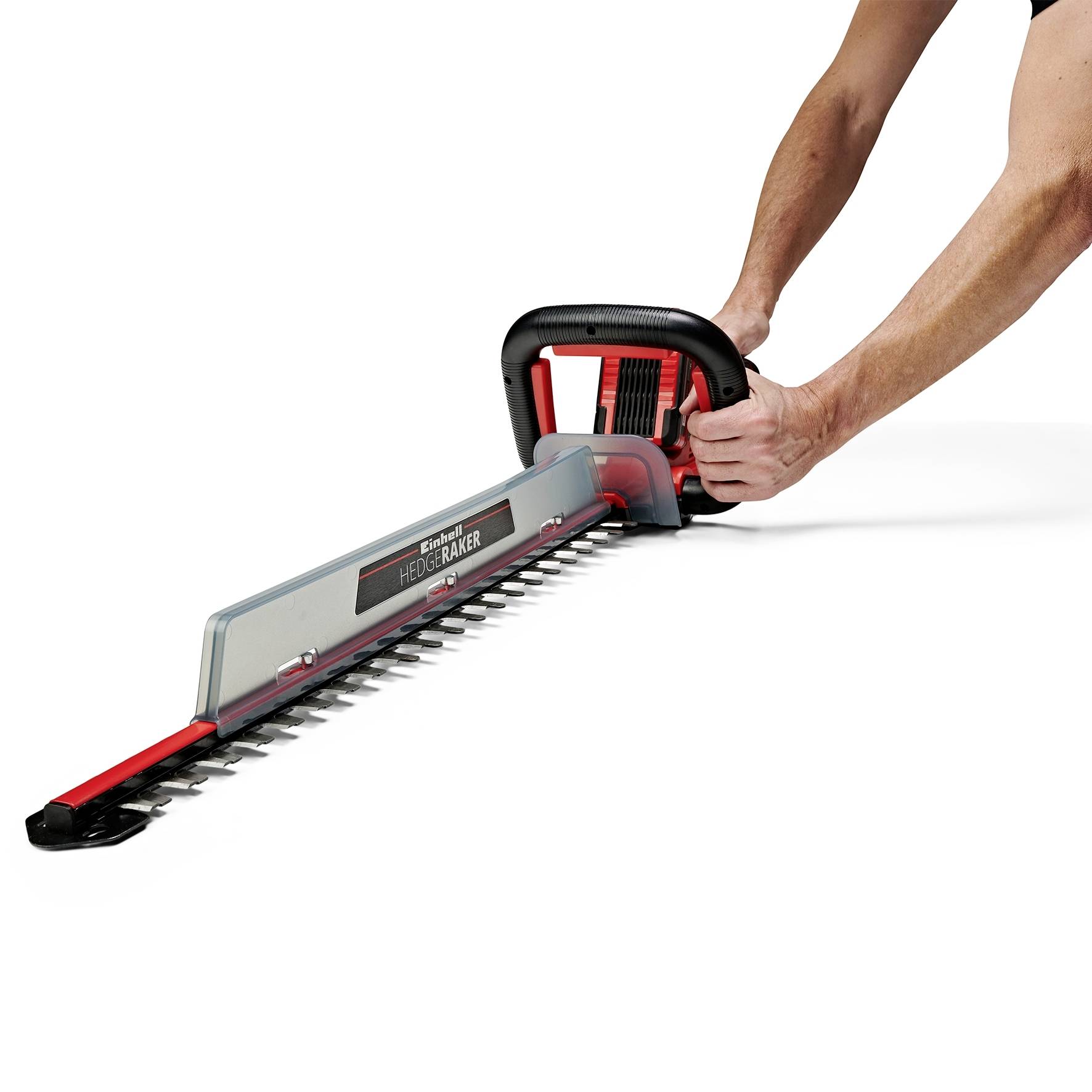 A person using an electric hedge trimmer, cutting a hedge. The device has a red handle and a silver blade.