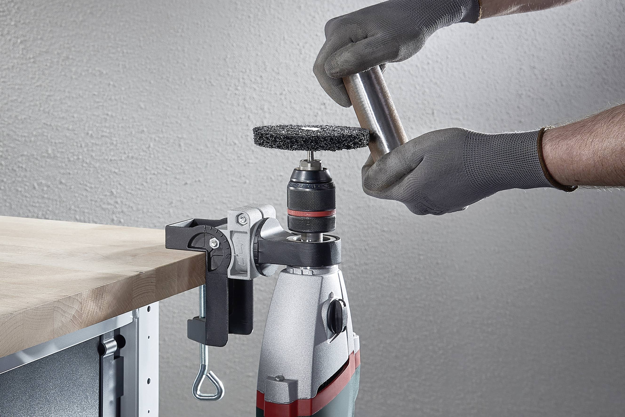 A person working on a metal rod in a vice while wearing gloves. A grinding attachment is being prepared.