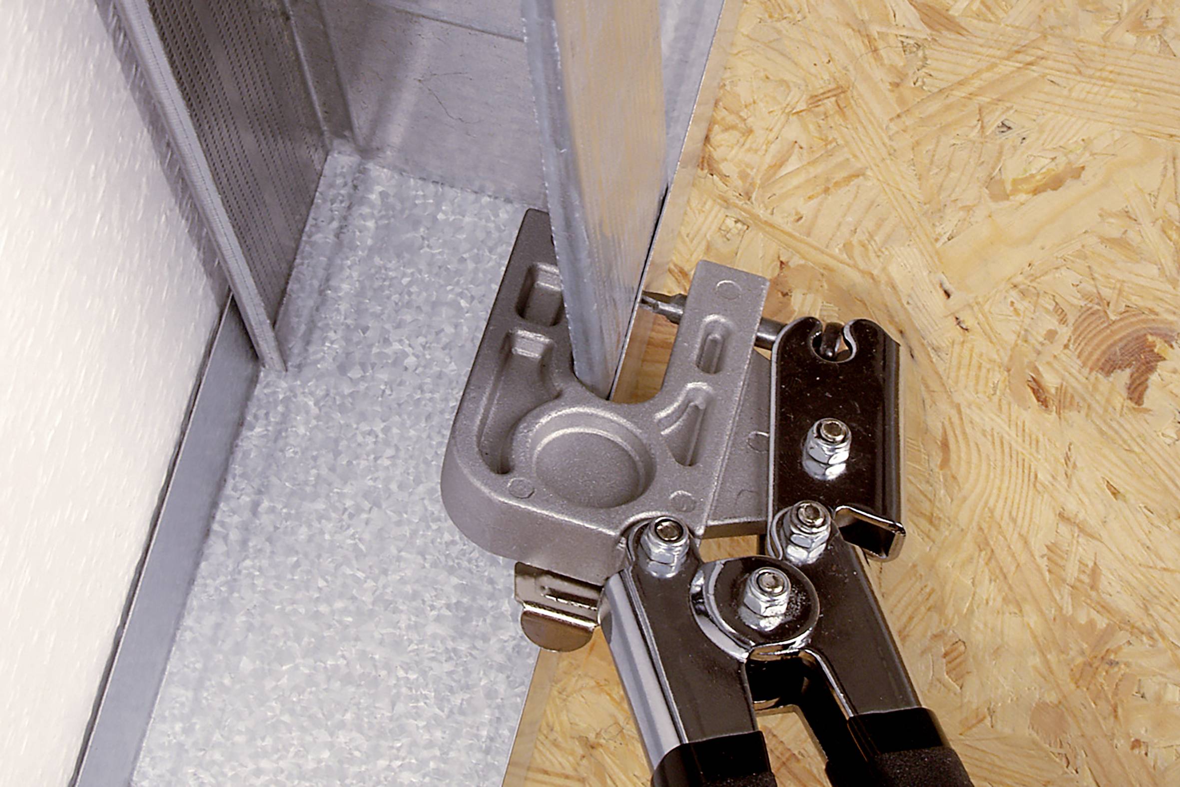 A tool clamp secures a metal profile to a wooden base plate in a construction context.
