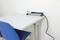 A blue chair is standing next to a white table, on which a power strip with plugged-in white cables is lying.