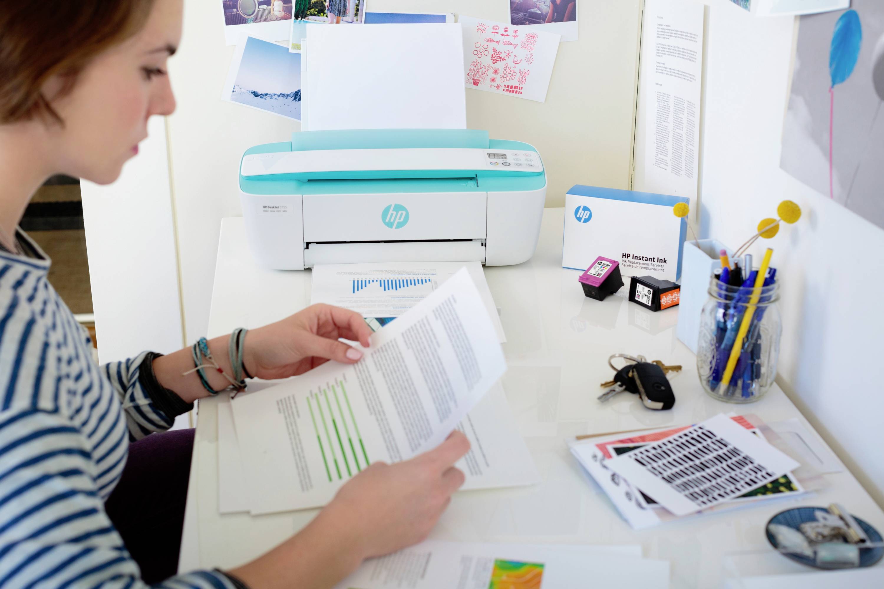 A person is sitting at a desk holding documents, while an HP printer prints documents in the background.