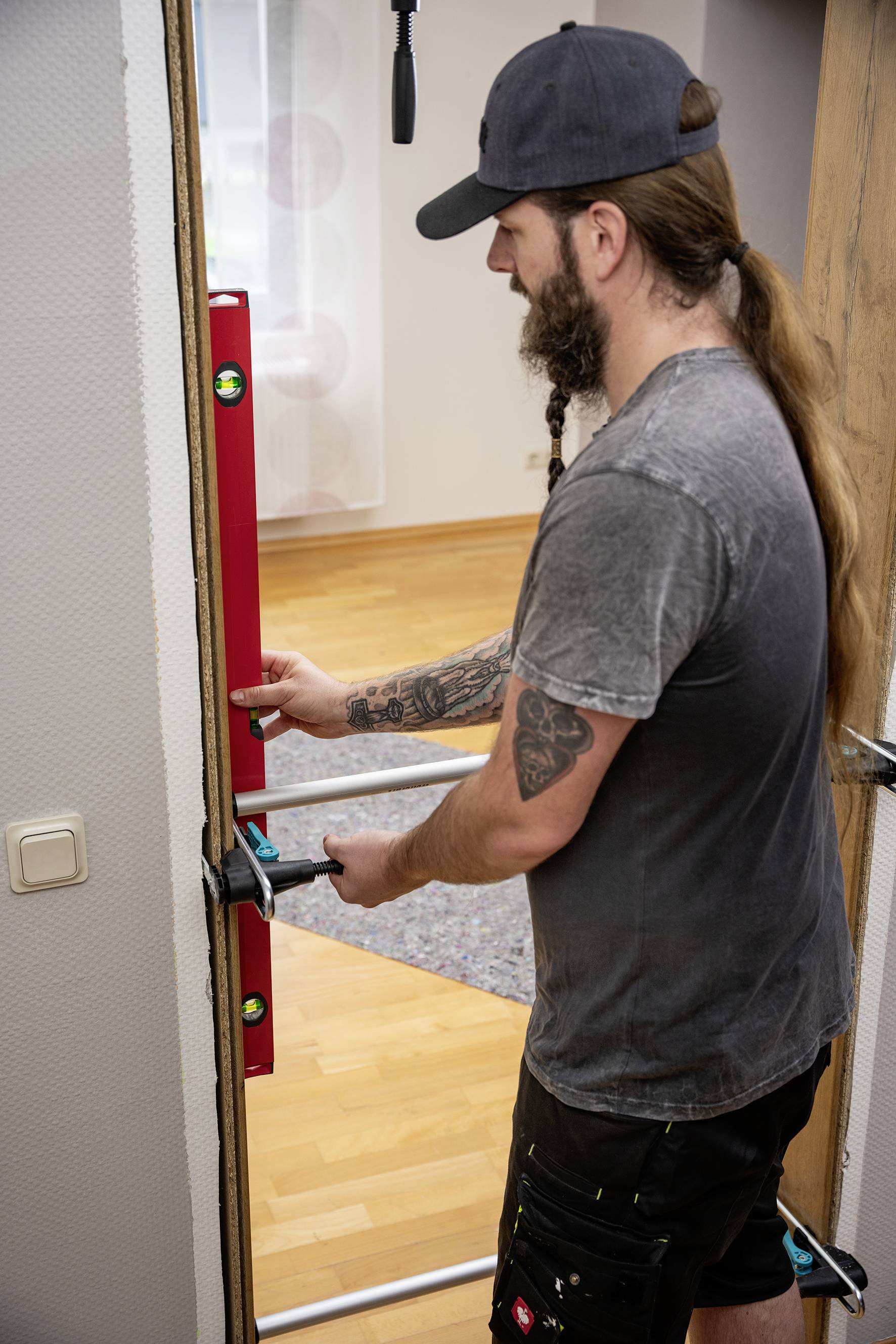 A person is installing a door frame in a room, holding a spirit level to check the alignment.