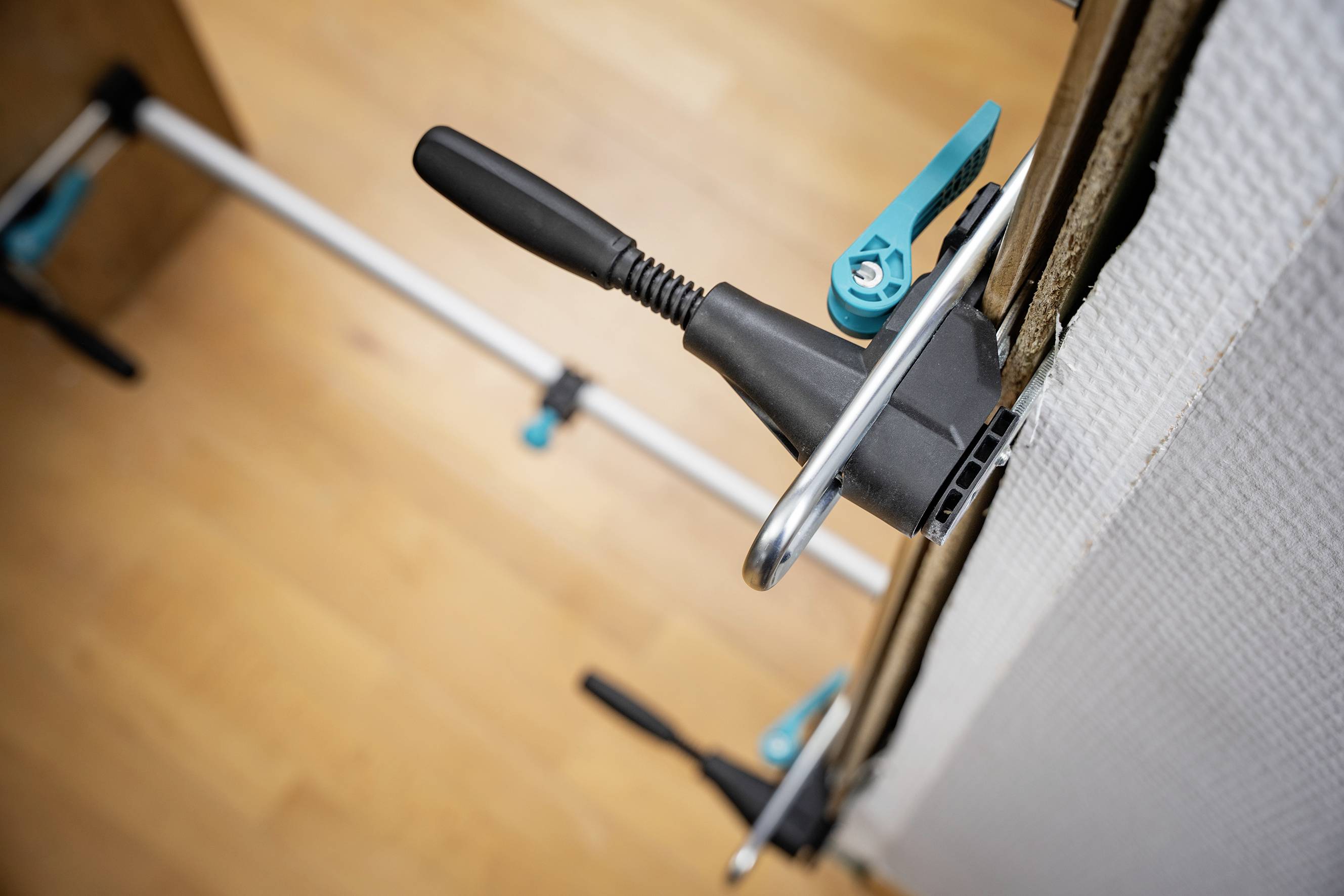 Fixing clips hold a wall panel securely to the metal frame. Wooden flooring visible in the background. Installation tools are in view.