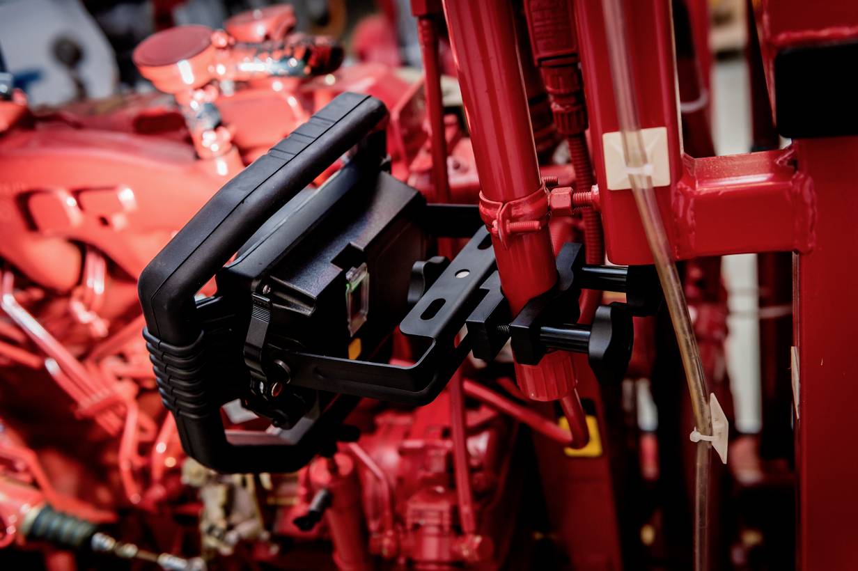 A black device with a handle positioned in front of a red machine component in an industrial setting.