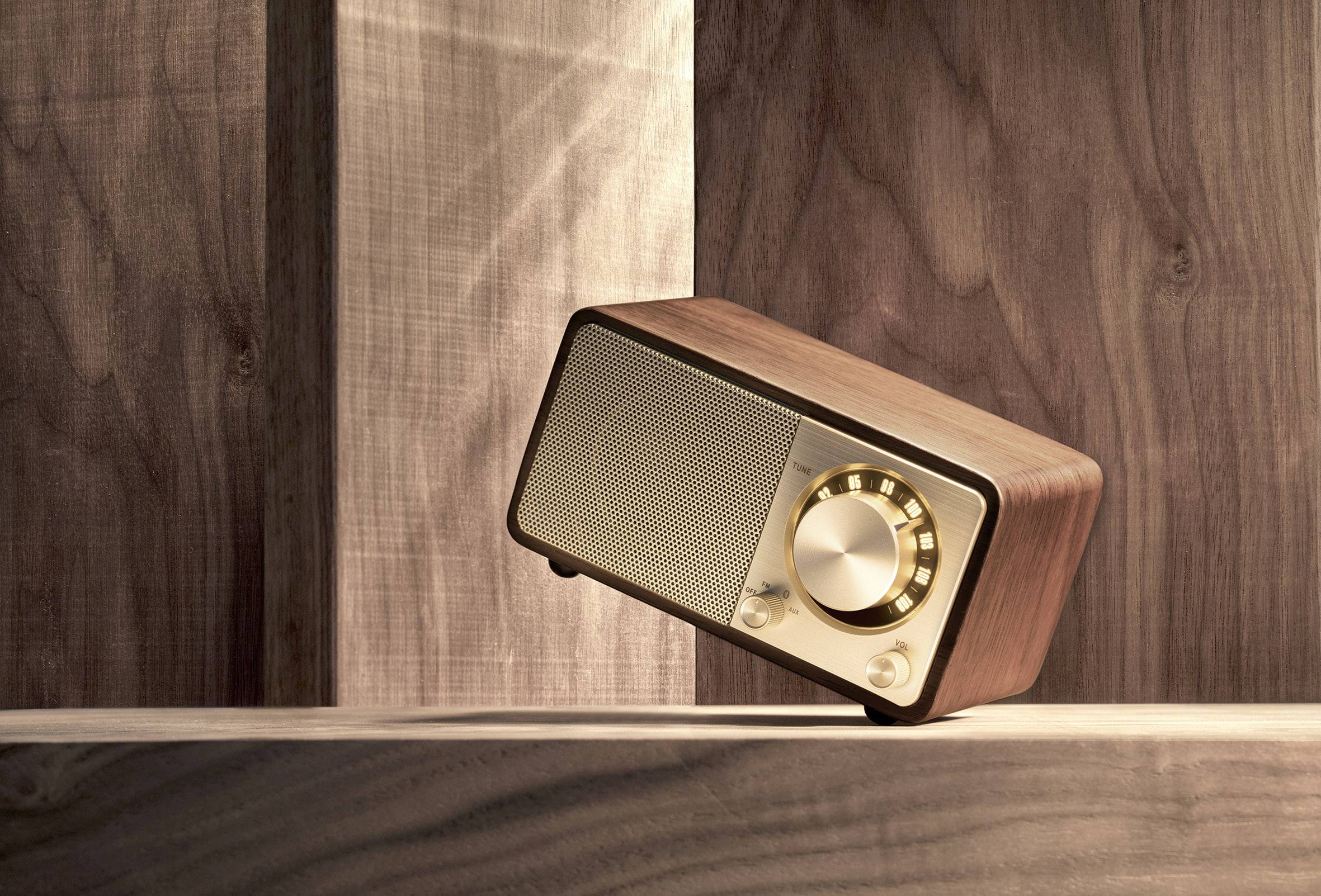 A vintage wooden radio with a golden knob sits at an angle on a wooden table, surrounded by warm, direct light.