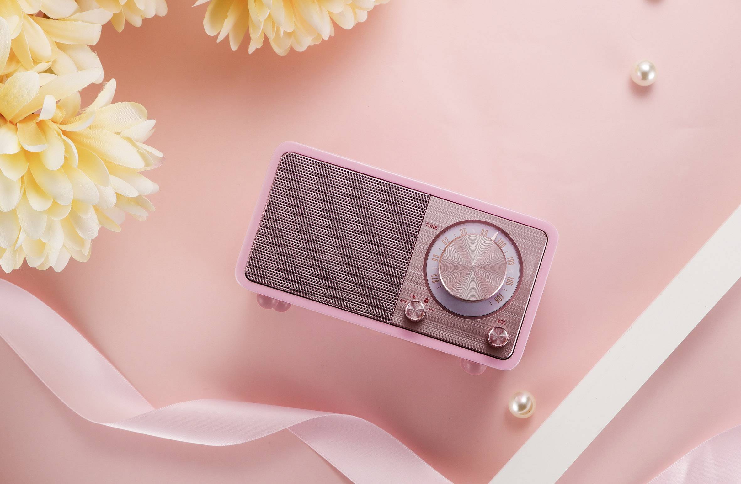 A pink retro radio on a pink background, surrounded by flowers and decorations, conveys a sense of nostalgia and style.