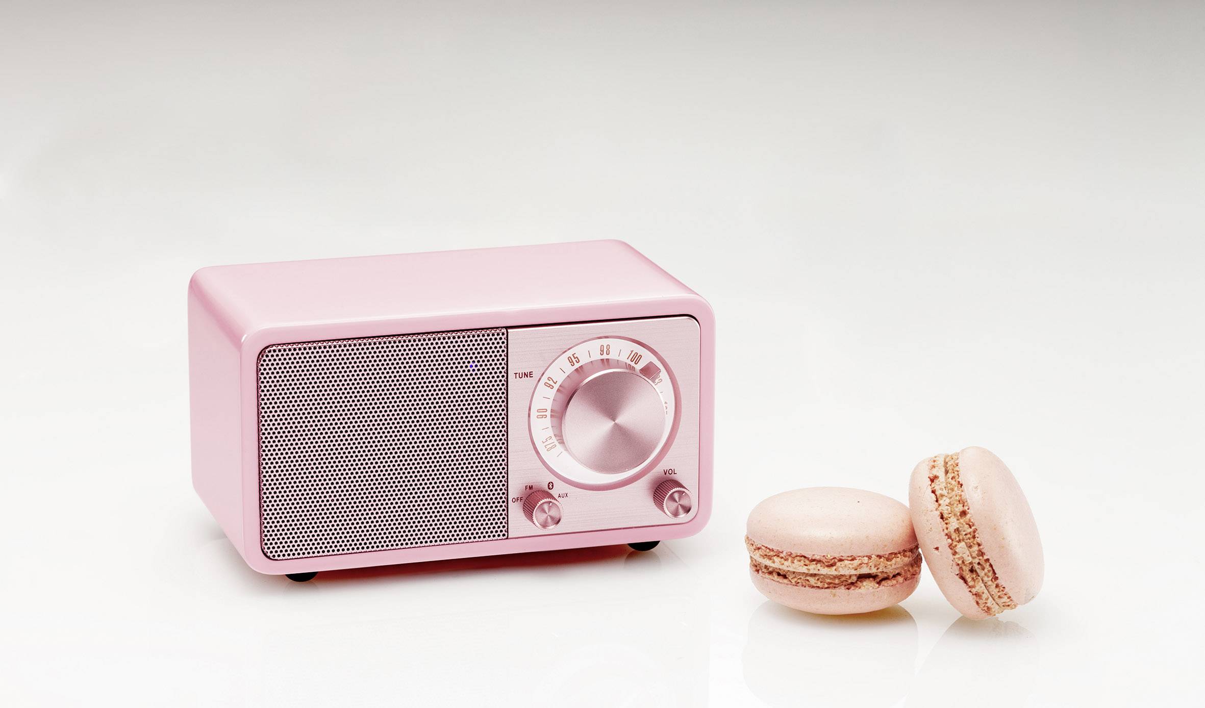 A pink retro radio with two pink macarons placed beside it, positioned on a light surface.