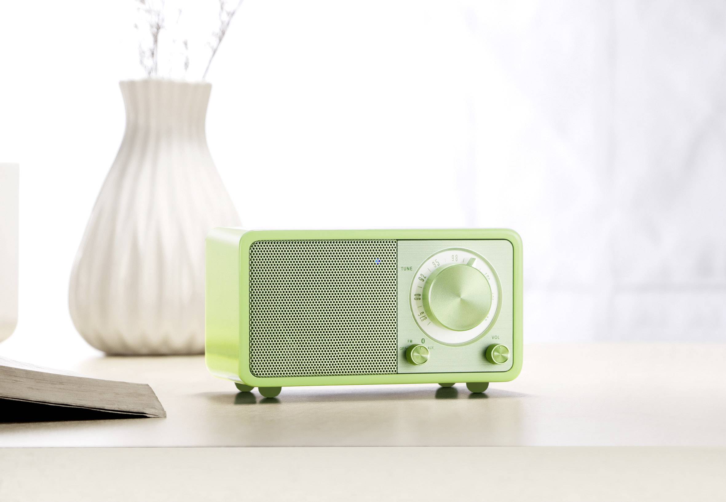 A pale green retro radio sits on a table in front of an elegant white vase.