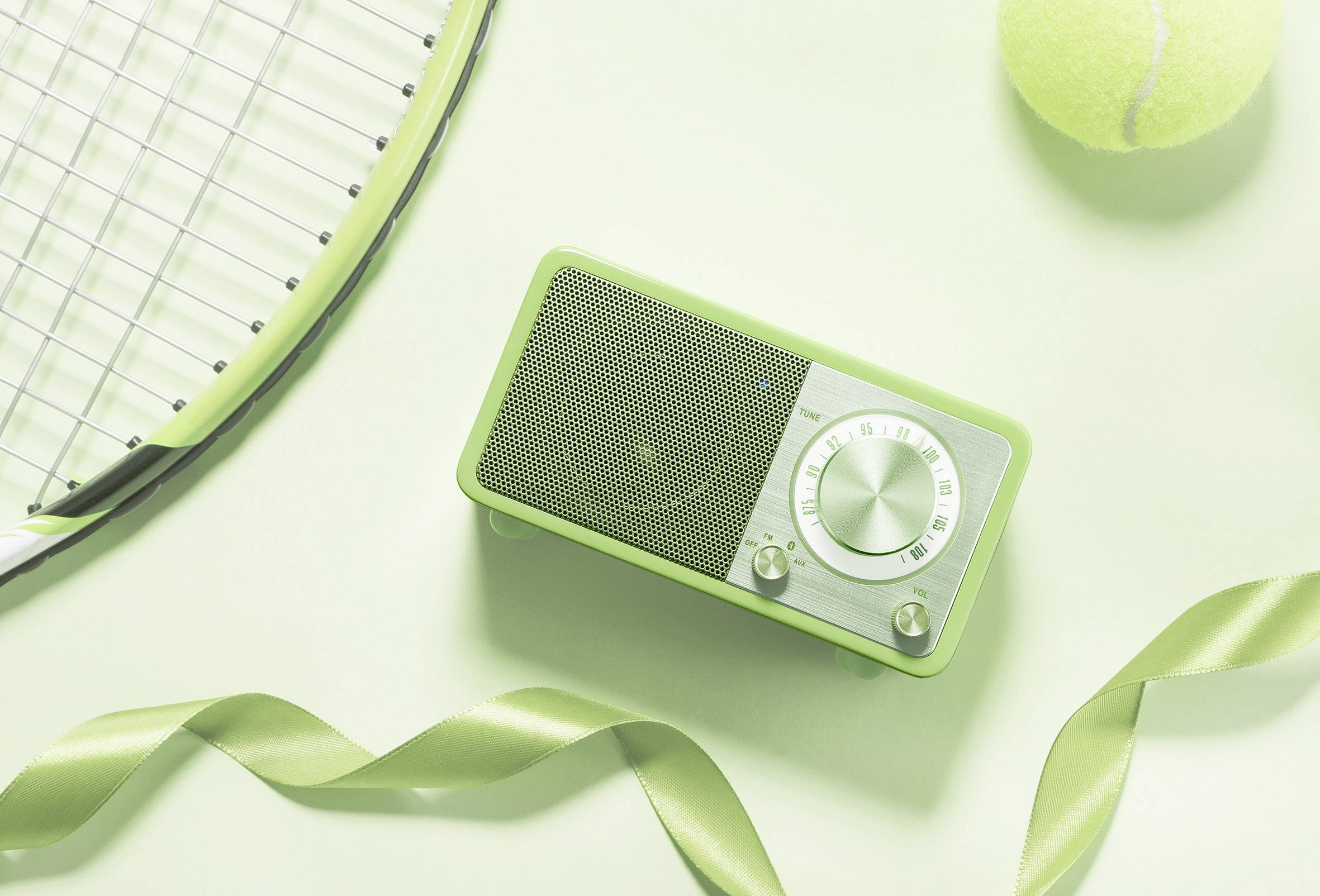 Retro-style radio on a light background with a tennis racket, tennis ball, and green ribbon. Sports and music united.