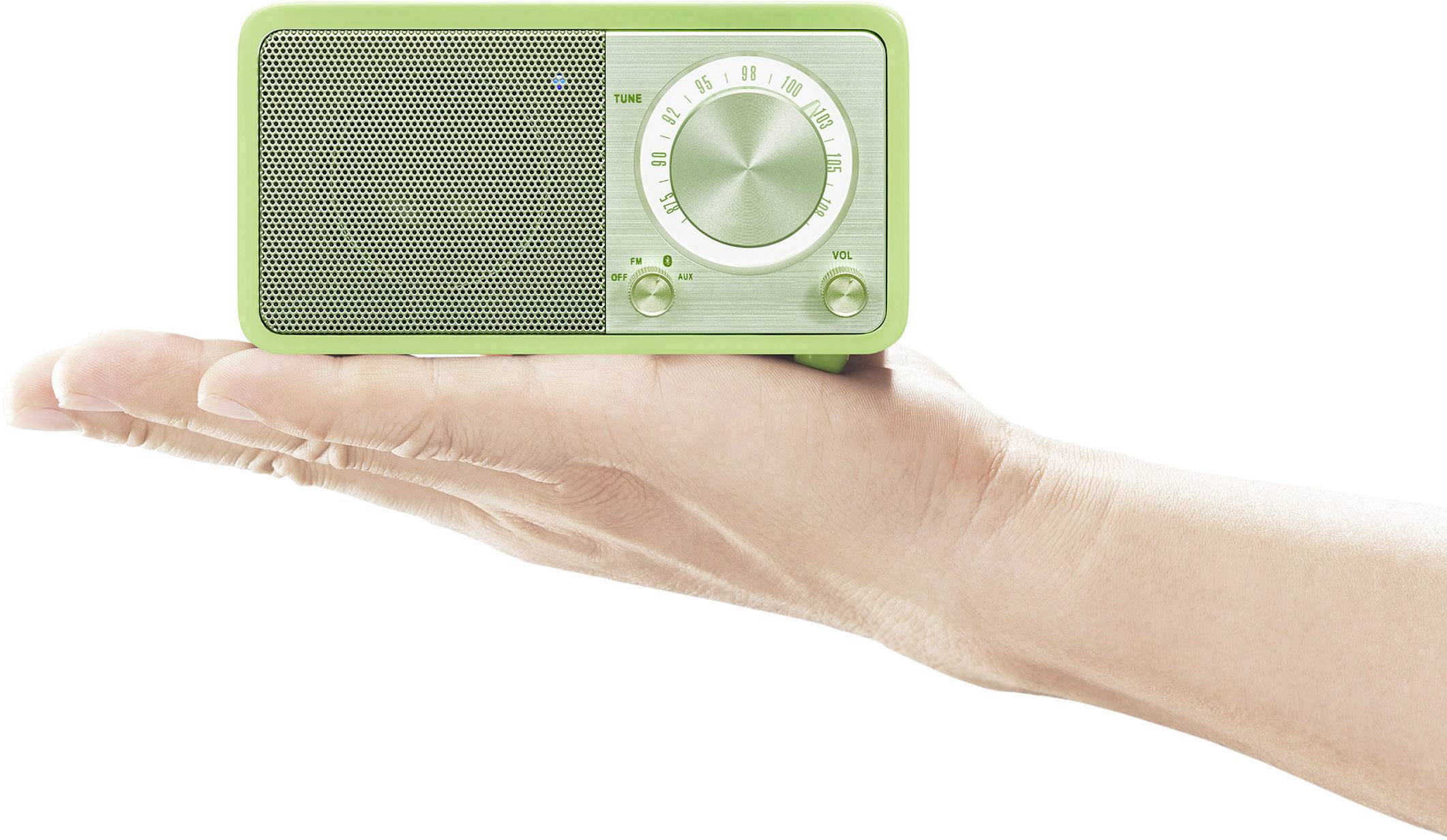 A hand is holding a small, green, portable radio with a volume control and speaker grille.