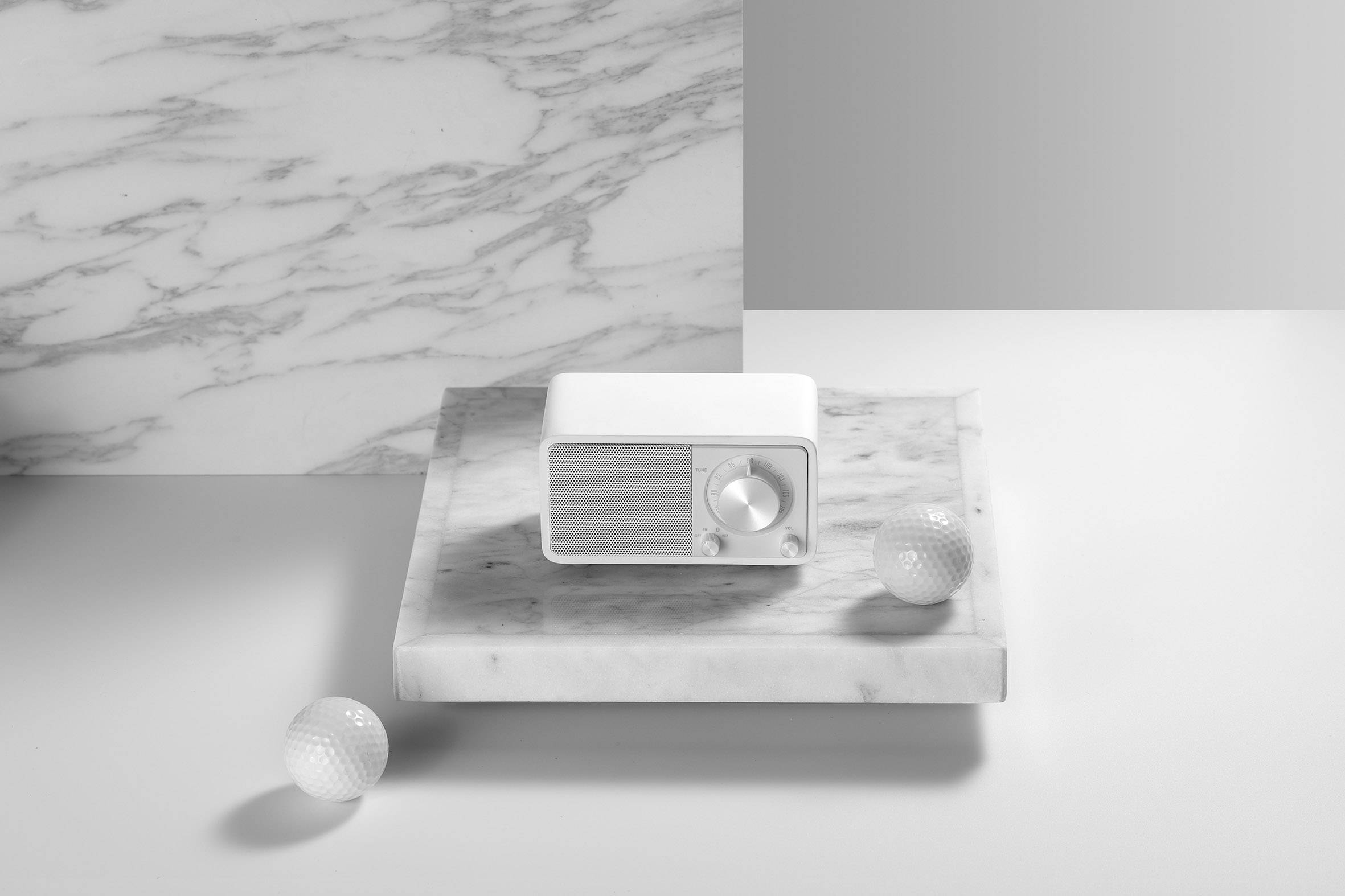 A small radio sits on a marble slab, surrounded by two golf balls. The background is also made of marble.