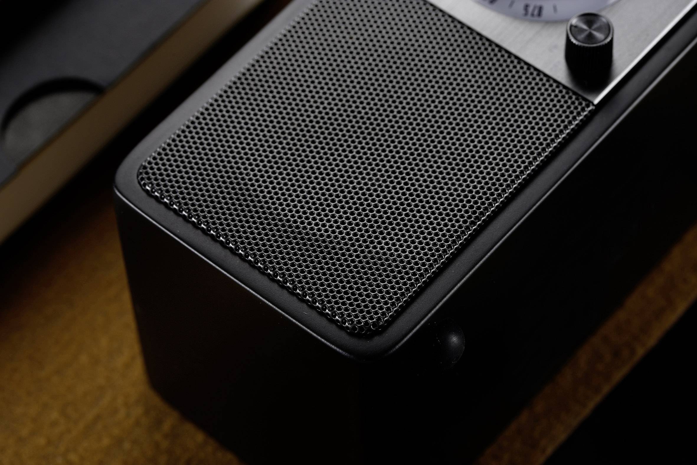 Black retro radio with visible speaker grille and a dial, placed on a wooden table.