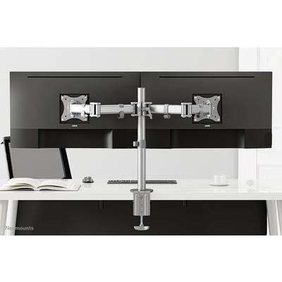 'Double monitor mount with two screens, attached to a white desk. An open book and a mug are in the background.'