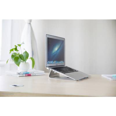 A laptop sits on a table with a stand, next to a pot containing a green plant. The screen displays a space background.