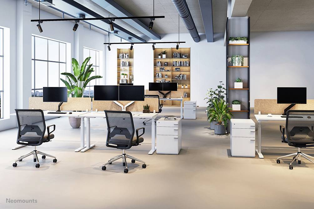 Modern office with multiple desks, office chairs and monitors, bright lighting, plants in corners, shelves on the back wall.